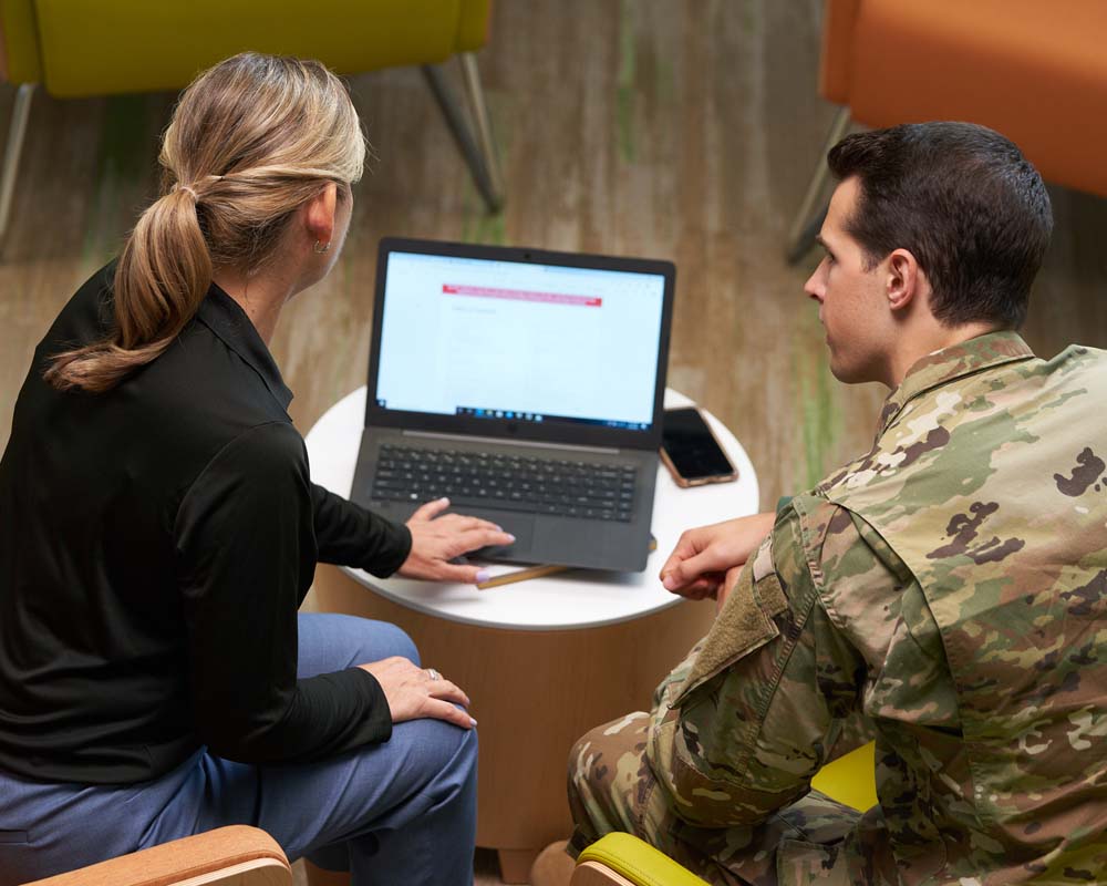 Two people, one in a military uniform, sitting and looking at a laptop.