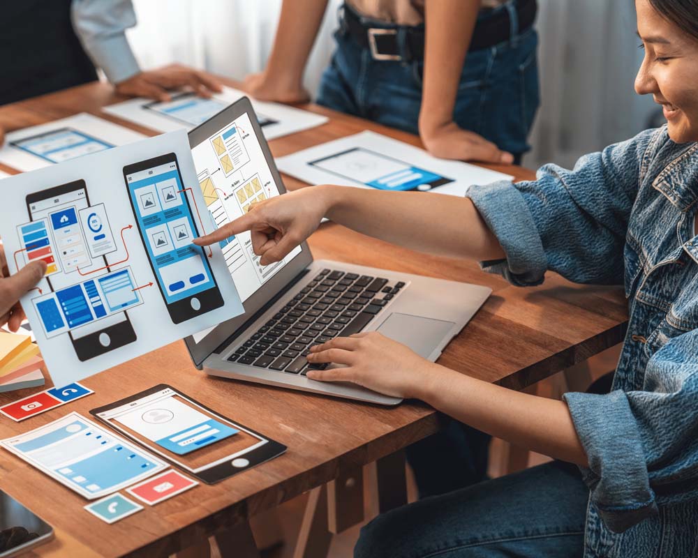 People around a table looking at colorful printouts and a laptop screen.