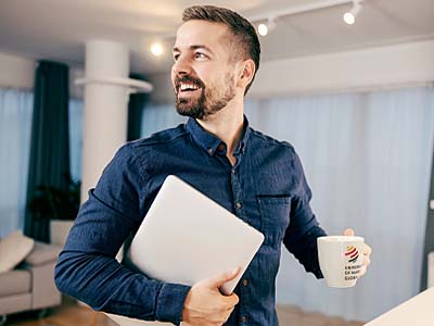 A man smiles in an office while carrying a laptop and UMGC mug.