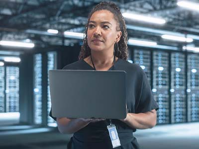 A woman in a server room on a laptop.