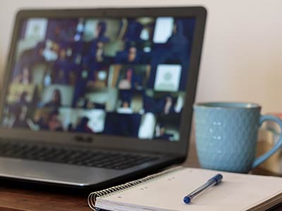Open laptop on a table beside a blue coffee mug and an open spiral notebook and pen