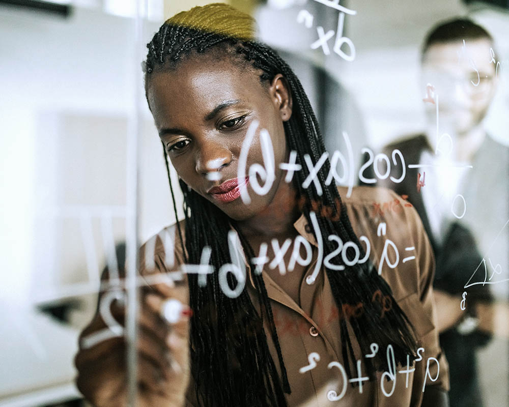 A person writing formulas on a dry erase board.