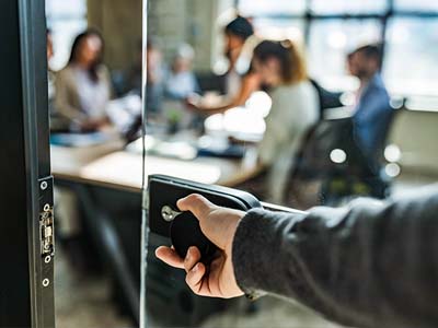 A hand opening the glass door to a conference room and behind it the blurred image of people sitting around a conference table