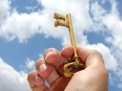 A person's hand holding a large key with the sky in the background.
