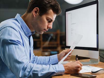 A person at a desk holding a piece of paper and writing notes.