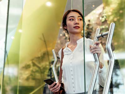 A person standing, looking serious, holding a cell phone in one hand and resting their other hand on a metal bar.