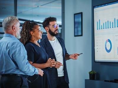 Three people looking at a large presentation screen with charts on it.