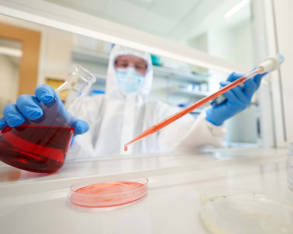 A person in a hazmat suit working with a red liquid in a beaker.