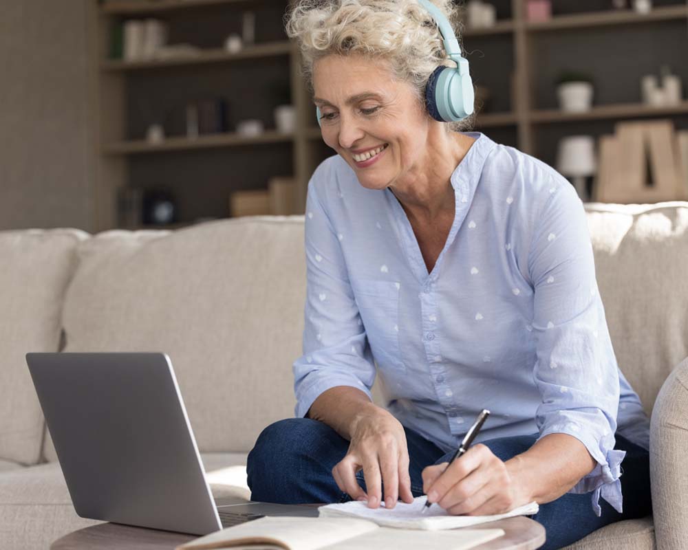 A person taking notes while smiling at a laptop.