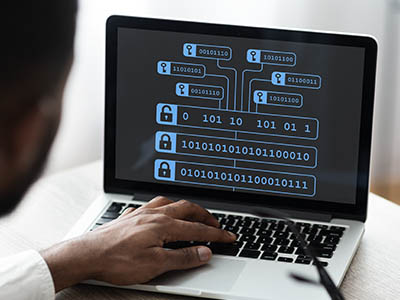 A person typing on a laptop displaying binary code.