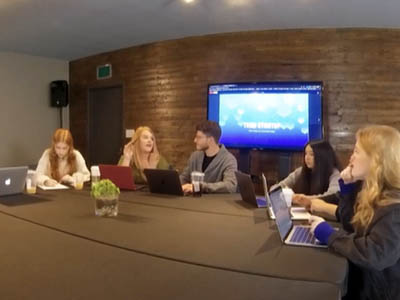 Five people sitting around a conference room table with laptops.