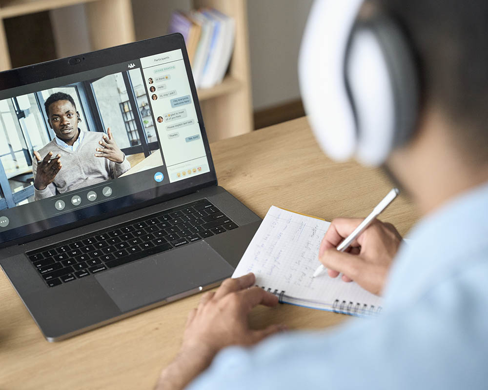 A person watching a video on a laptop and taking notes.
