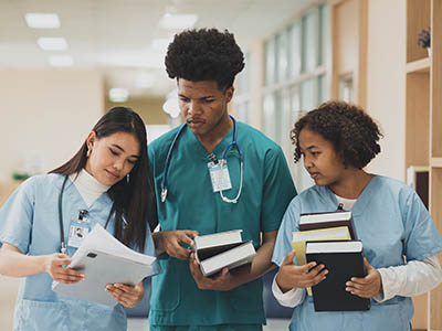 Three people in scrubs standing and holding books.