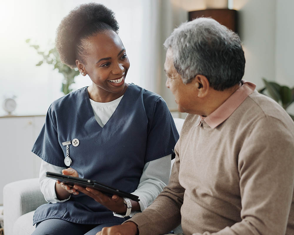 A person in scrubs holding a digital tablet and talking to another person.