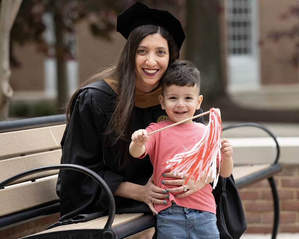 A person in graduation regalia and a small child smiling.
