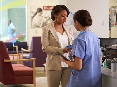 A person in a suit talking to a person in medical scrubs in a hospital setting..