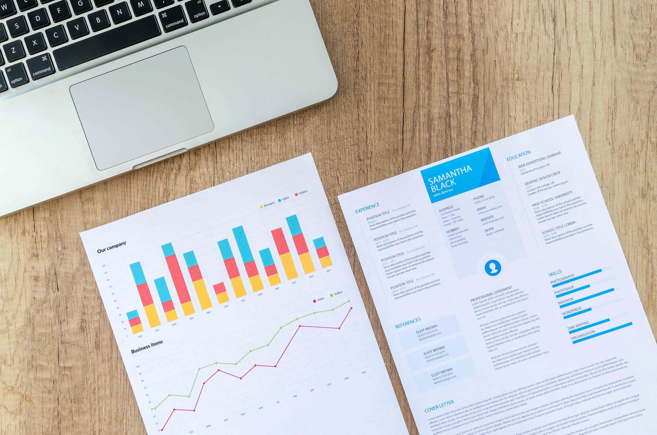 Two pieces of paper next to each other. The first shows a bar graph and line graph about 'our company' while the second shows a resume.