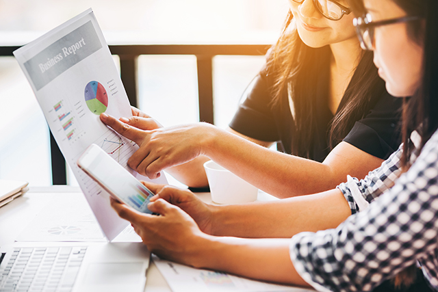 Two business woman investment consultant analyzing company annual financial report balance sheet statement working with documents graphs. Concept picture of economy, market, office,money and tax.
