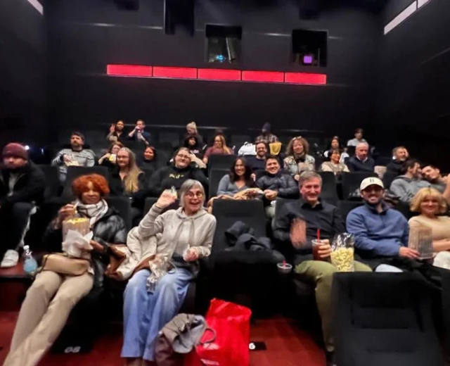 UMGC students and community members sit in a darkened movie theater before a film screening, some holding popcorn.