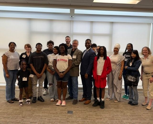 Two executives with a group of about 15 student participants and their Big Brothers Big Sisters mentors in a conference room at UMGC headquarters.