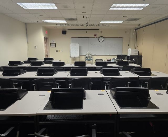 Photo of a room with several lines of tables. The tables have computers for testing embedded in them.