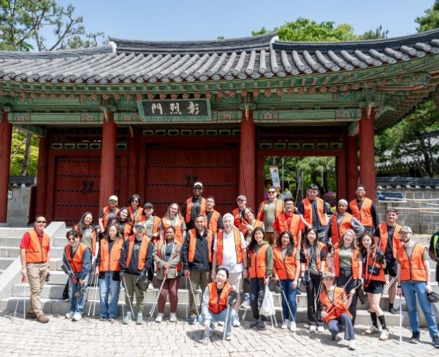 A group of about 30 people in orange vests with litter grabbing sticks at Hyochang Park in Seoul.