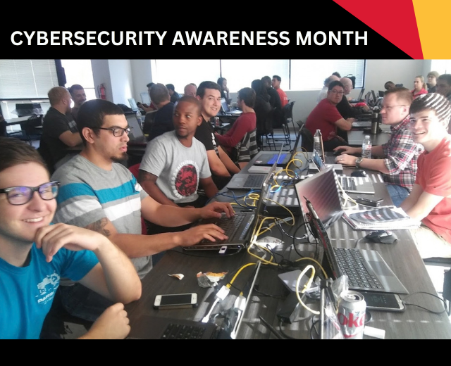 “Cybersecurity Awareness Month.” Six young men with laptops sit across from each other at a long table during a cyber competition, with other similar groups in the background.