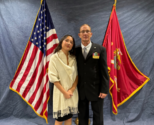 Sierra Parzyck and her father, Stephen pose in front of American and Marine flags in formal attire. Marine veteran Stephen Parzyck is wearing service medals.
