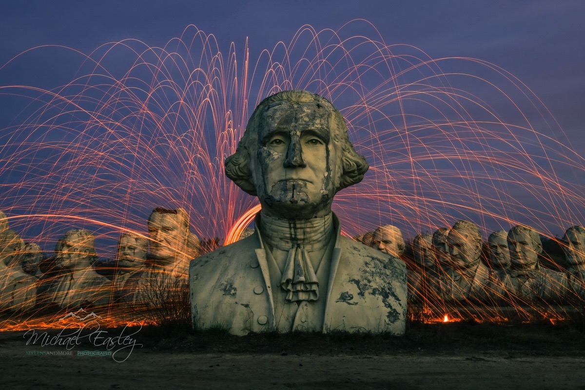 A statue of George Washington with fireworks behind it.