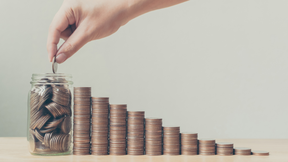 A series of stacks of coins leading up to a jar with multiple coins saved in it.