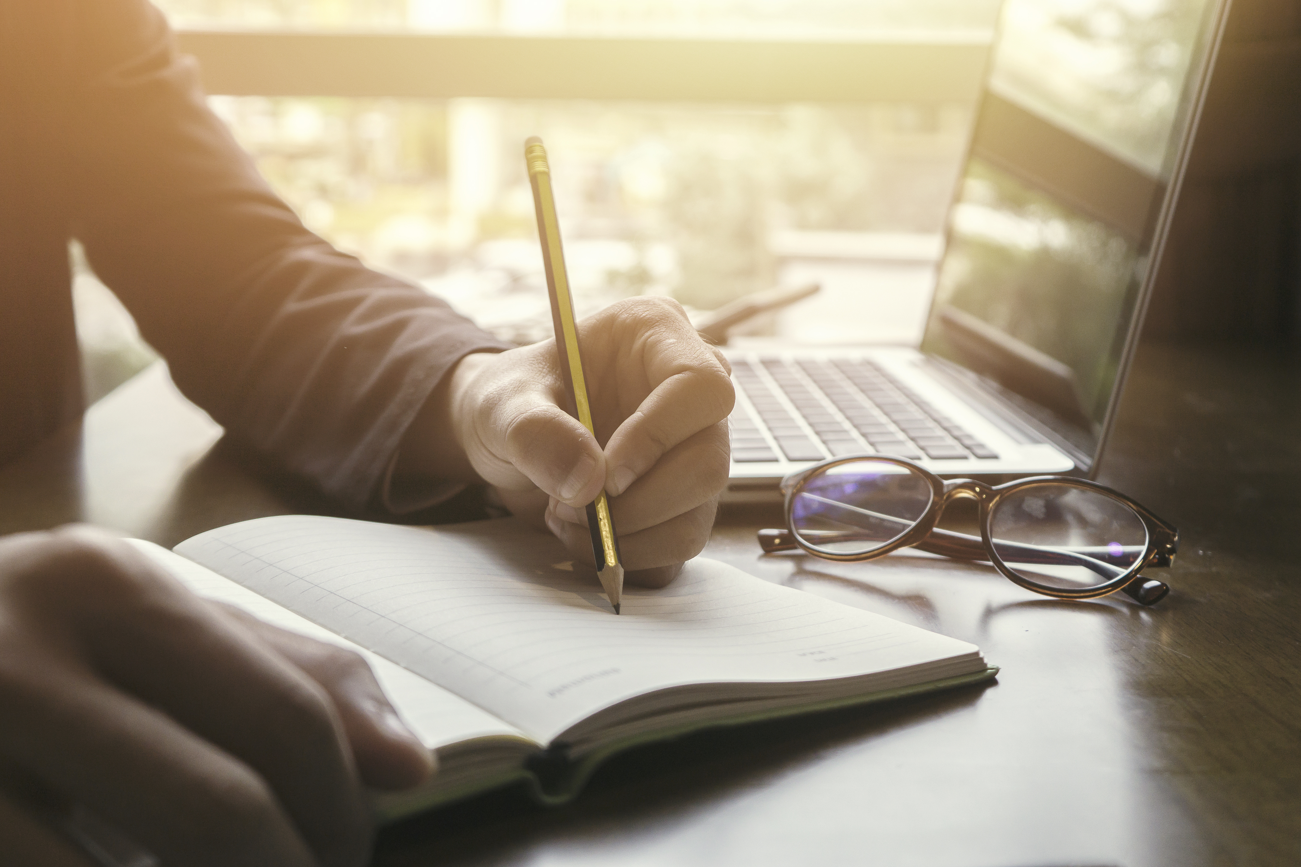 A person taking notes in front of a laptop.