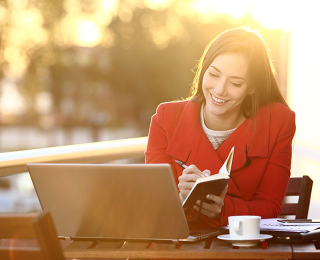 A woman taking notes at a laptop outside.