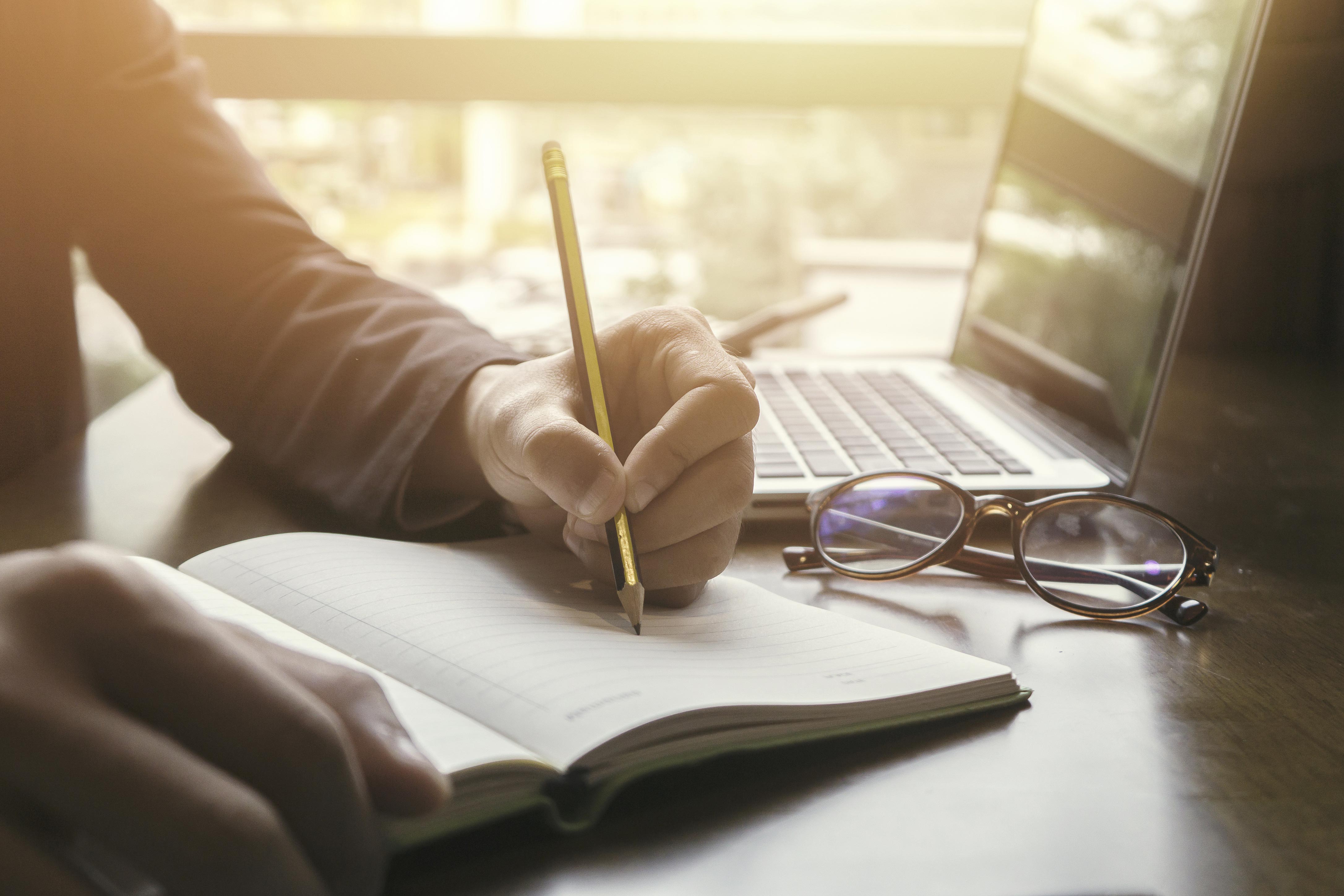 A person taking notes in front of a laptop.