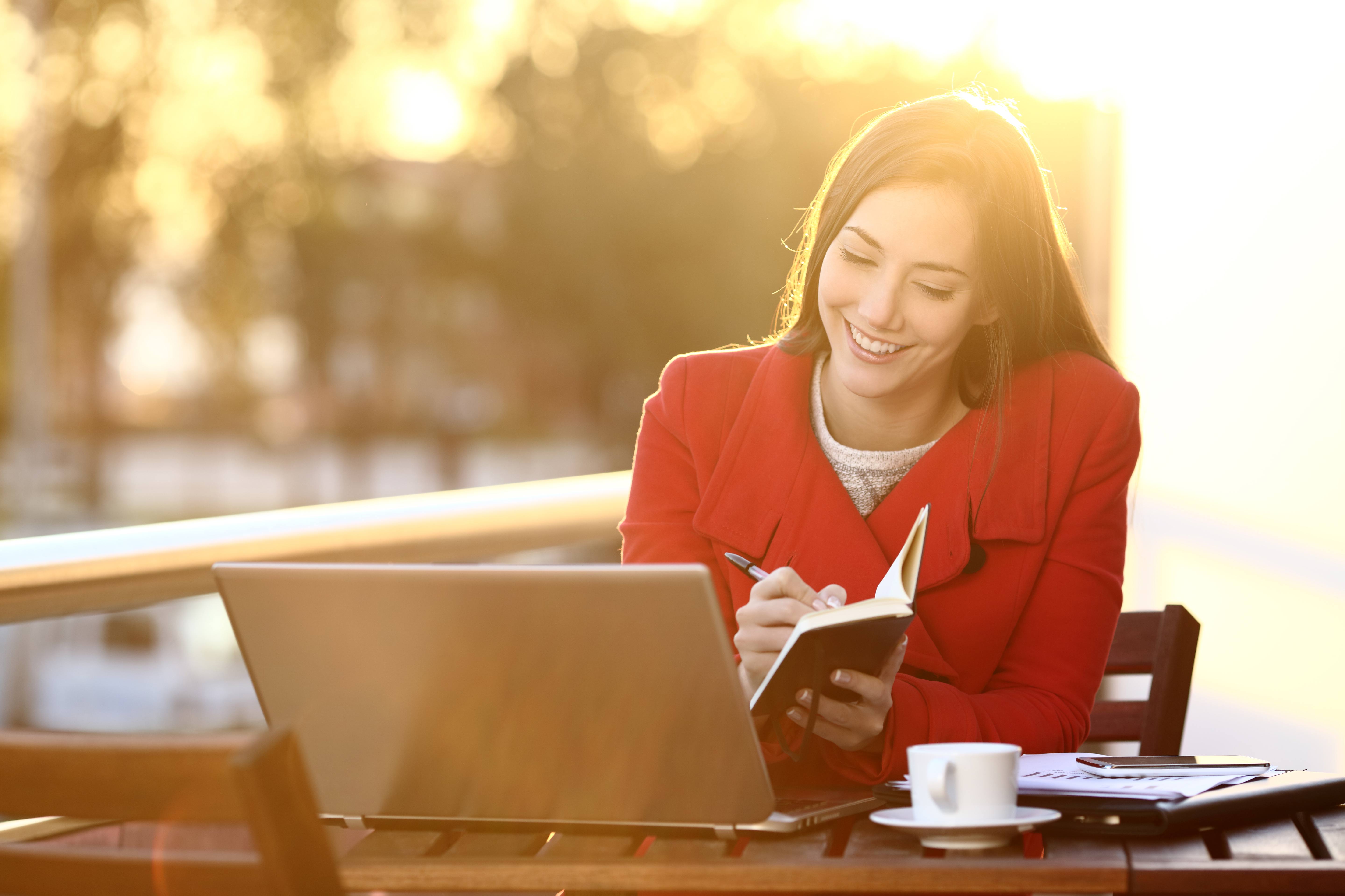 A woman taking notes at a laptop outside.