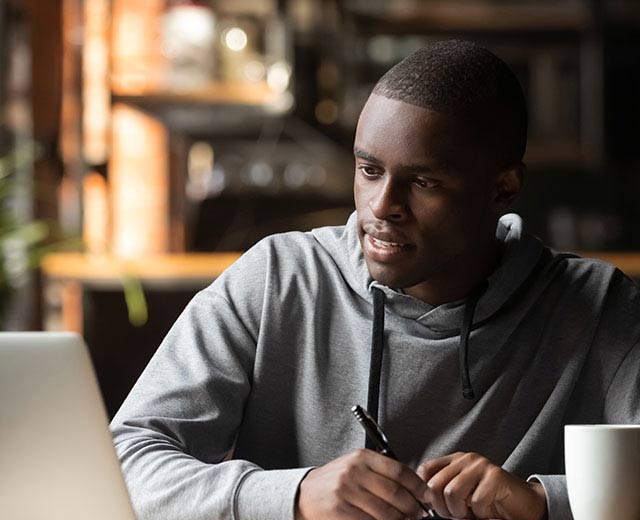 A person looking at their laptop while taking notes in a notebook.