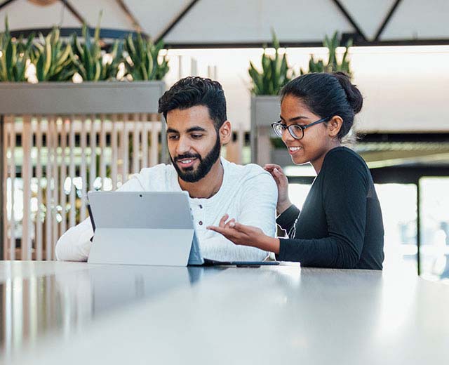 A man and a woman sitting down in front of a tablet computer.