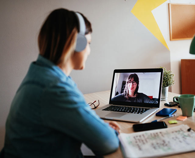 A person wearing headphones is video conferencing with another person on their laptop.