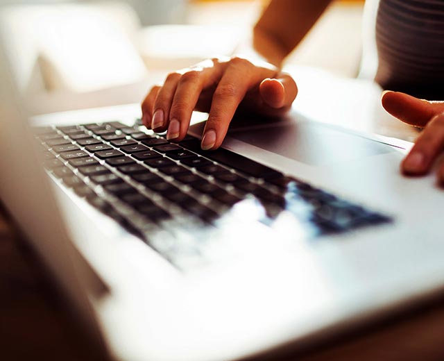 A closeup of two hands typing on a laptop.