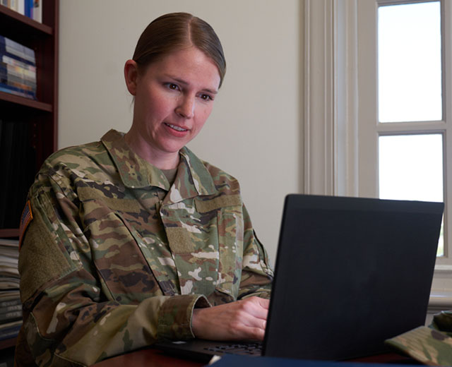 A person in uniform looking at a laptop screen.