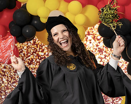 A woman in a graduation gown joyfully celebrating her achievement.