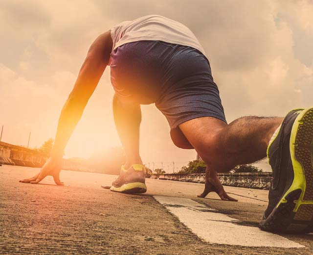 A runner in a starting stance about to race into the sunlight.