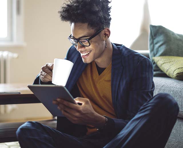 A person smiling while holding a mug in one hand and a digital tablet in the other.