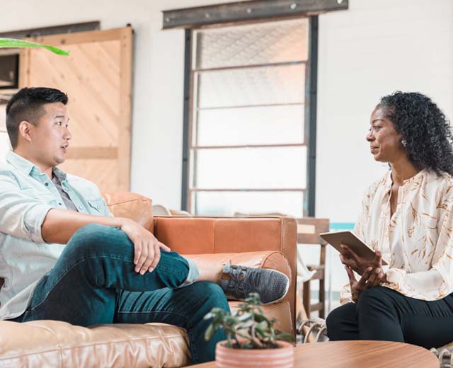 Two people sitting and talking; the person on the right is holding a tablet.