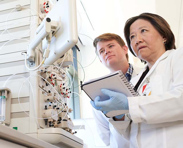 Two people in lab coats looking at a computer screen.