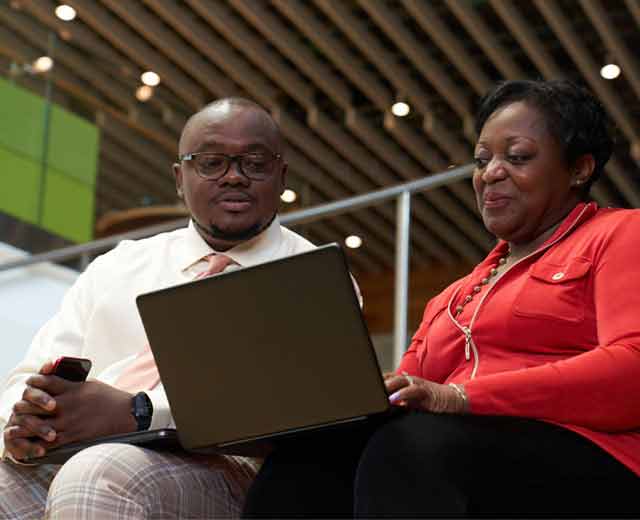 Two individuals sitting down looking at a laptop.