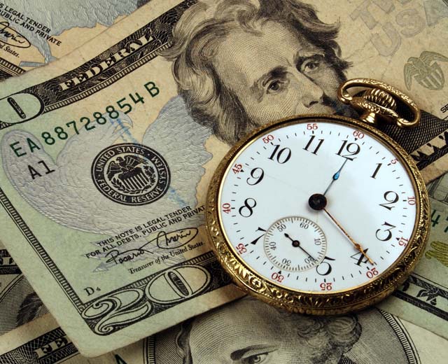 A gold pocket watch lying on top of a twenty-dollar bill and other bills.