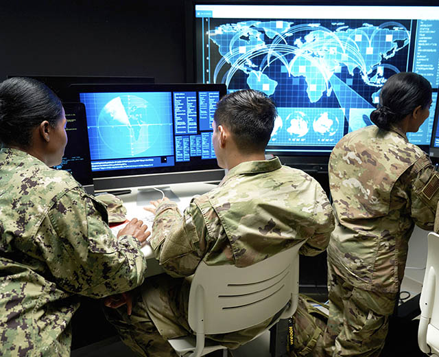Three people in military uniforms looking at computer monitors.