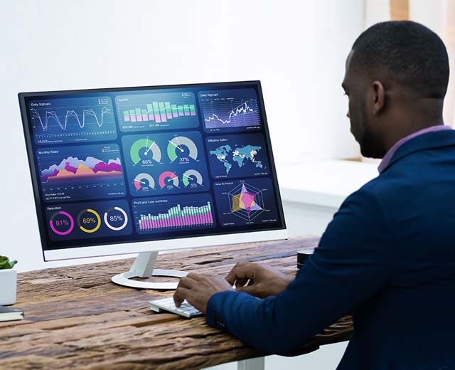 A person looking at a computer monitor with several graphs and charts on it.