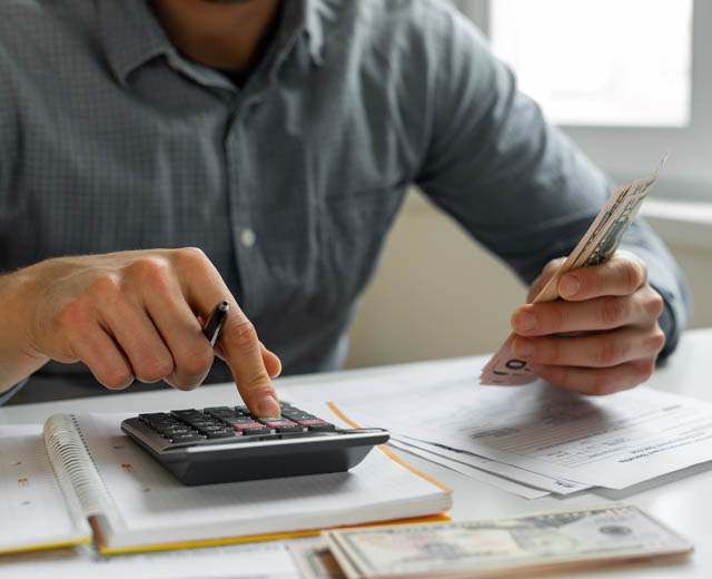 Image of a man counting money with a calculator.