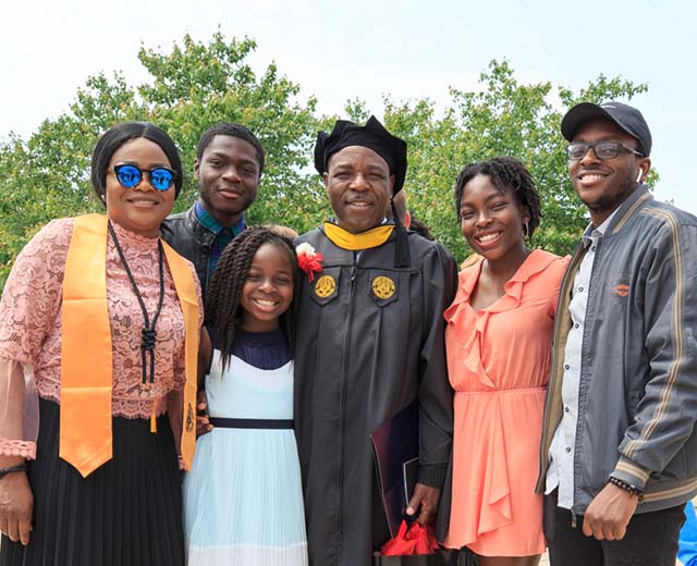 A man in a graduation cap and gown poses for a photo with his family.